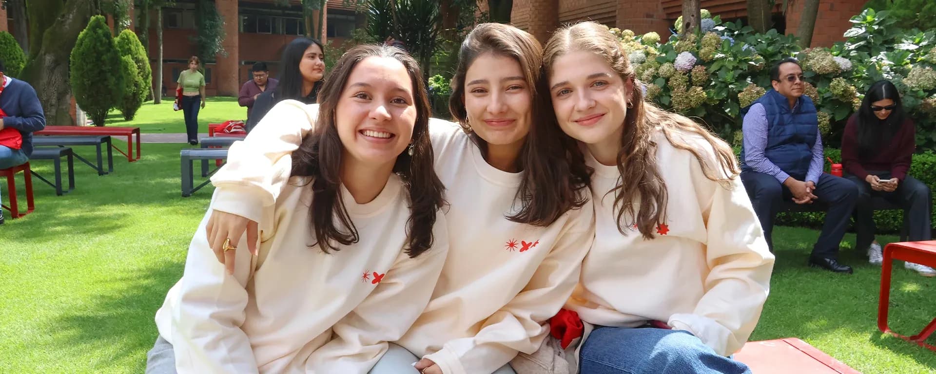 Tres estudiantes de la IBERO posan sonrientes frente a la cámara en los jardines centrales de la IBERO.